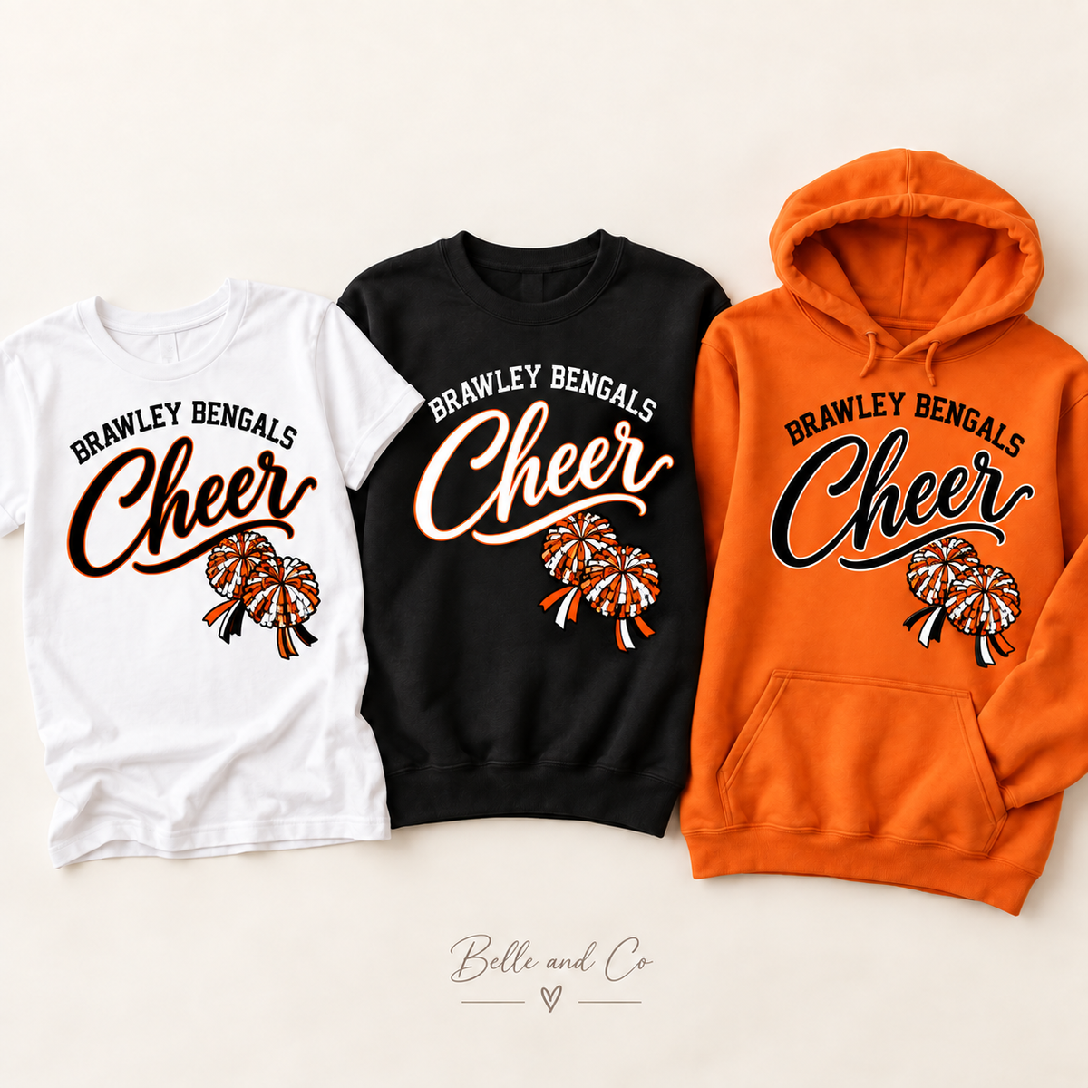 Brawley Bengals Cheer Game Day Darling with smaller diagonal pom-poms below Cheer lettering on a white tee, black crewneck, and orange hoodie
